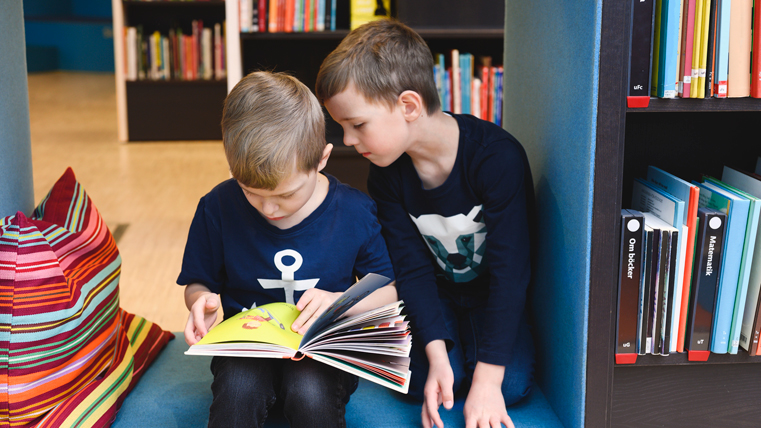 Två unga pojkar bläddrar i en bok på ett bibliotek