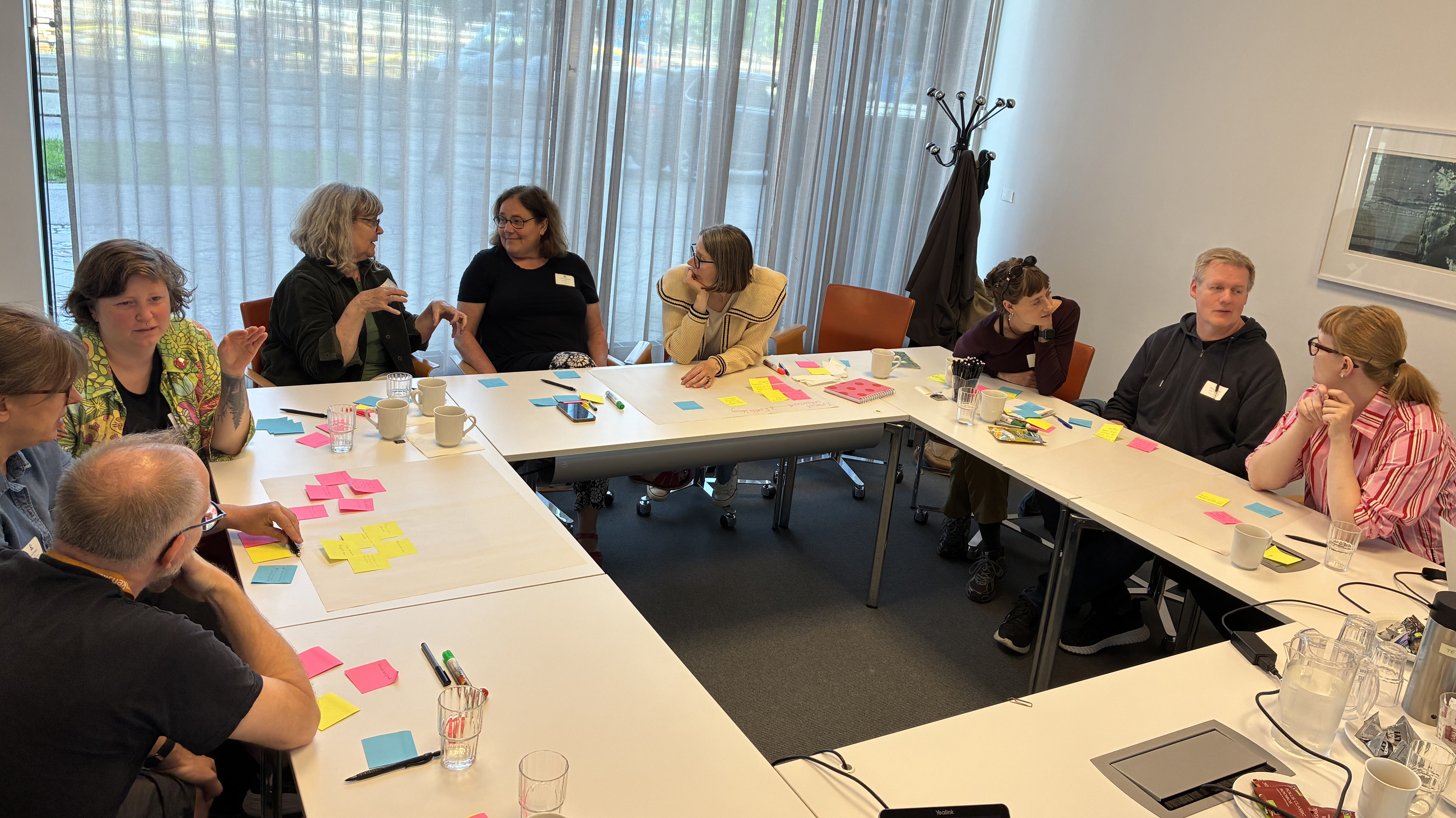 Nio bibliotekarier sitter runt ett bord med post it-lappar framför sig på bordet.