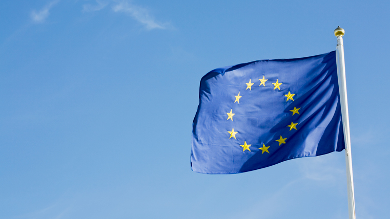Den blå EU-flaggan med gula stjärnor i ring fladdrar mot en blå himmel