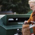 Man har parkerat sin cykel vid återvinningsstationen där han håller på att lägga in tidningar. 