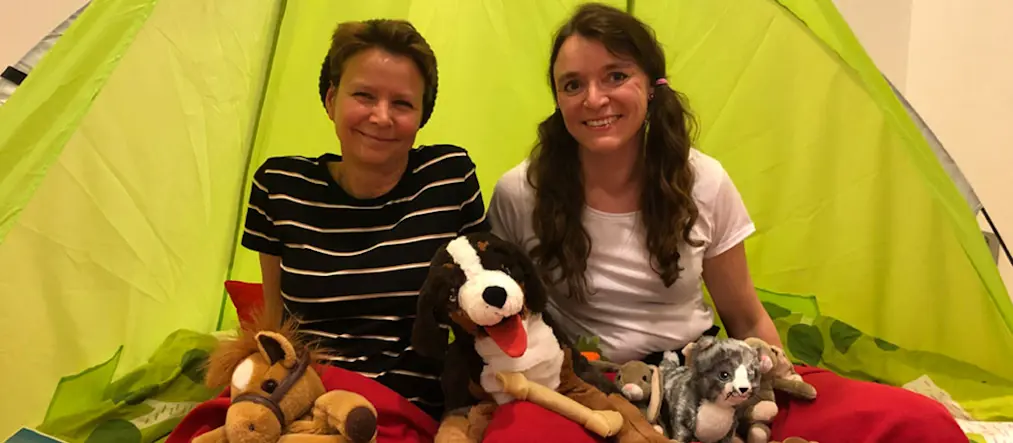 Två kvinnor sitter inne i ett tält tillsammans med flera gosedjur.