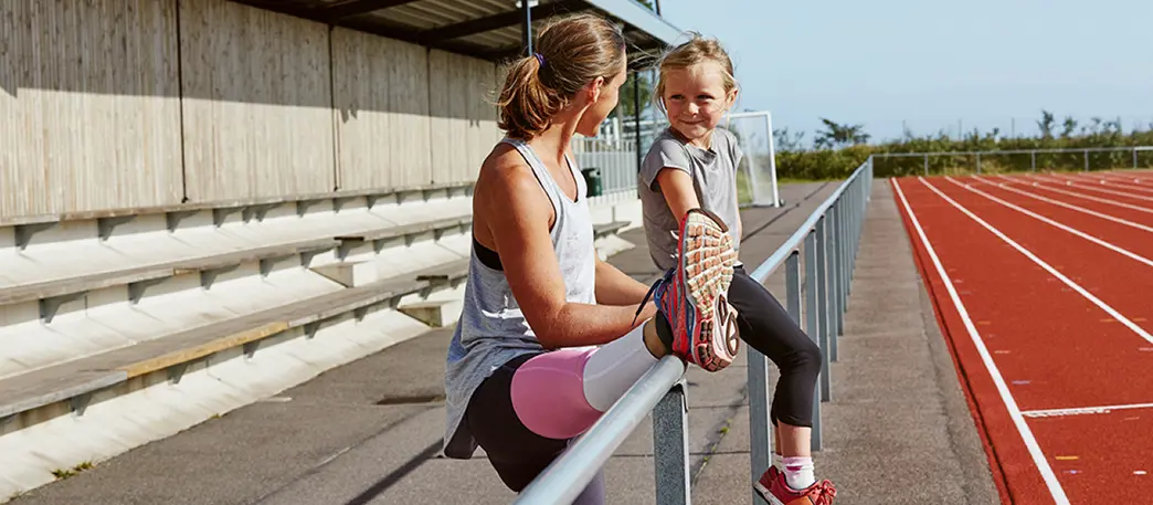 Mamma och barn stretchar på en löparbana utomhus.