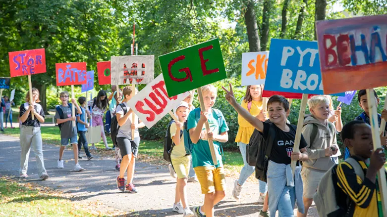 Fotografiet föreställer barn som går i ett demonstrationståg med plakat. Det är sommar, barnen är glada och de går igenom en park.