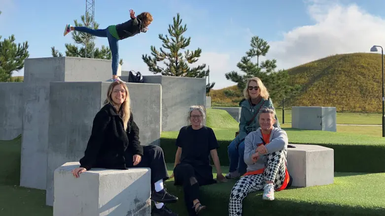 Fyra kvinnor sitter i en park och en balanserar på ett ben i bakgrunden