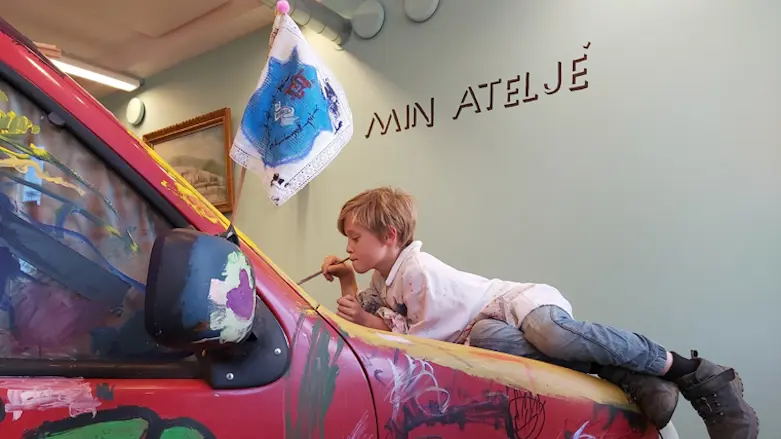 En pojke ligger på motorhuven på en bil och målar på bilen