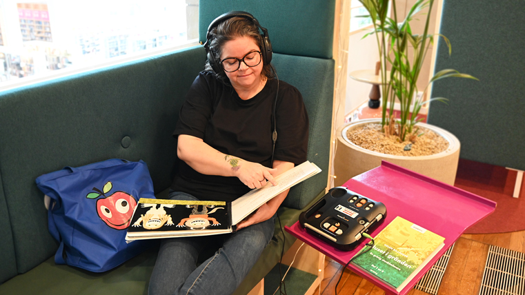 En kvinna med hörlurar sitter i en soffa och läser en bok