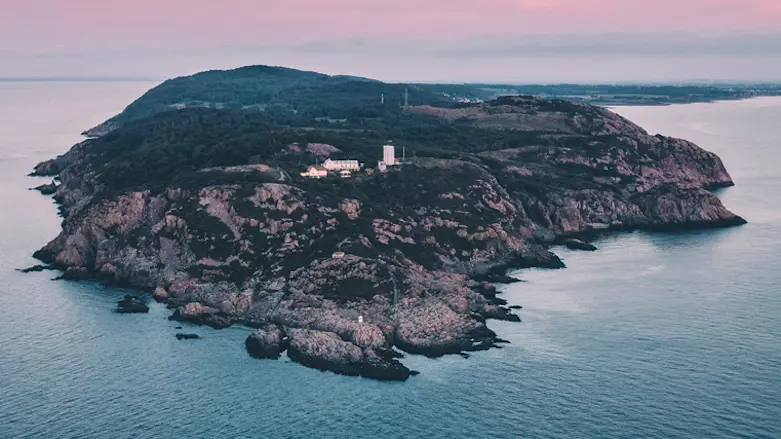 Flygbild över Kullaberg som är en stenig udde med en fyr på toppen. Himlen är rosa och havet stilla.