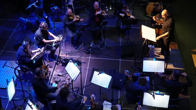 Musiker med olika instrument sitter på stolar i en ring. Var och en har ett notställ framför sig.