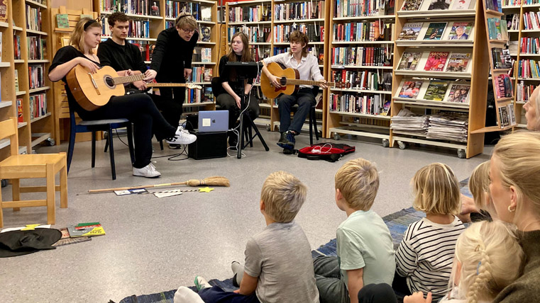 Ungdomar som spelar instrument i biblioteksmiljö med förskolebarn i publiken.