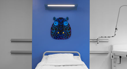 Ett målat flodhästhuvud på en blå vägg bakom en sjukhussäng.