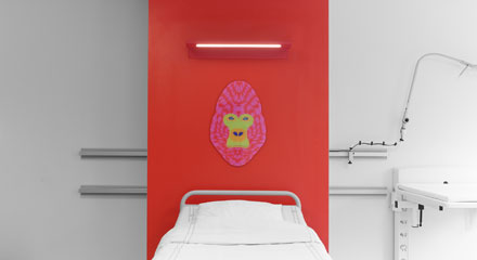 En röd vägg med en rosa målad gorilla bakom en sjukhussäng.