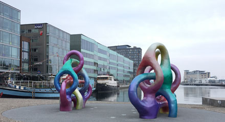Två färgglada konstverk framför en kanal i stadsmiljö.