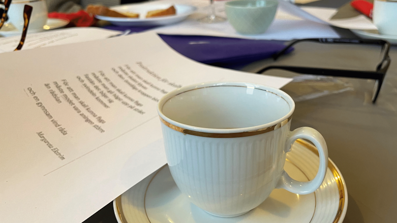 Ett papper med en dikt och en vit kaffekopp på ett bord.
