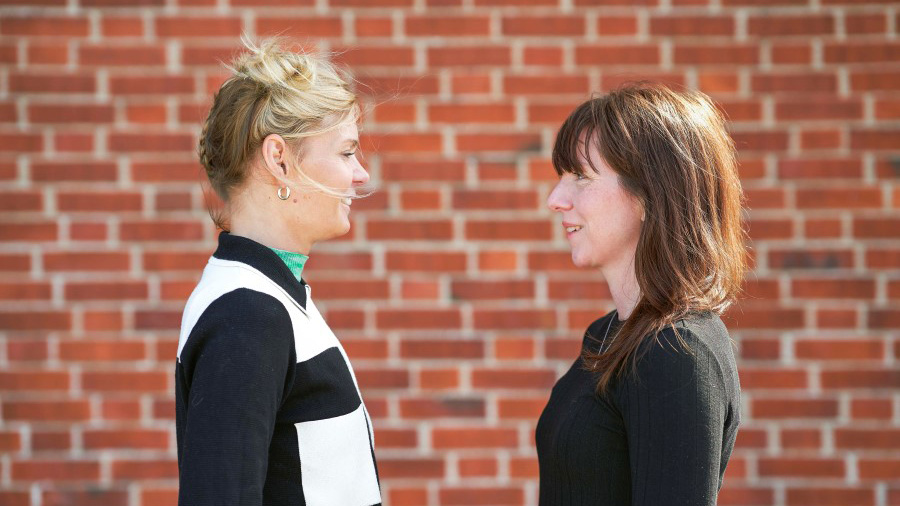 Karin och Kajsa som gjort Formgivarpodden framför en tegelvägg.