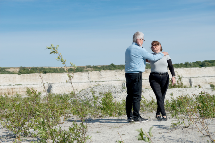 En äldre man och kvinna dansar tilsammans i ett sandigt landskap.