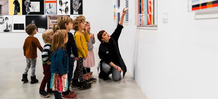 En kvinna pekar på ett konstverk. En grupp barn tittar på vart hon pekar.