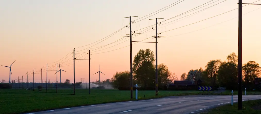 Elkablar och vindkraftverk mot rosa solnedgångshimmel.