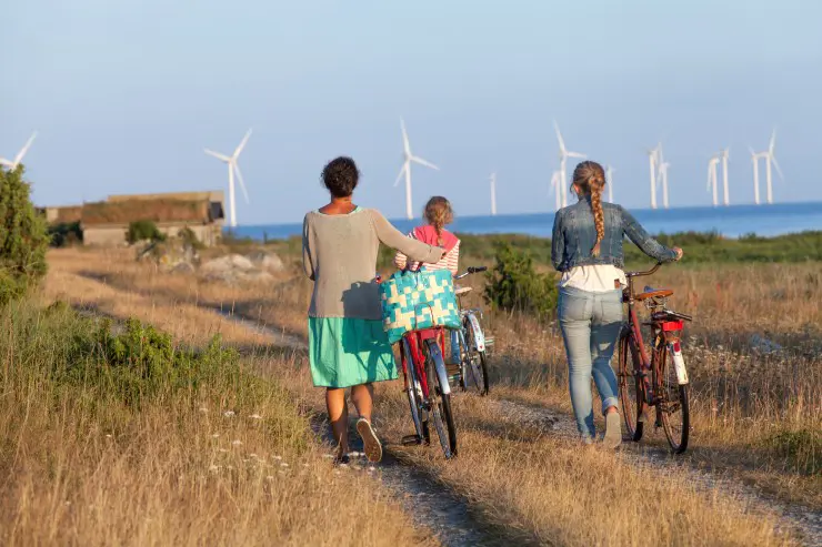 Kvinna och barn går med cyklar över äng.