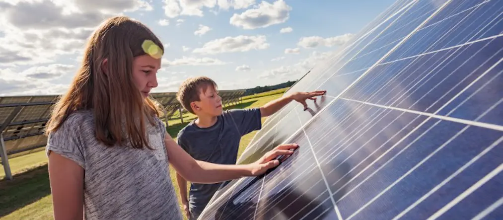 En flicka och en pojke lägger sin hand på en solcell. De är utomhus och solen skiner.