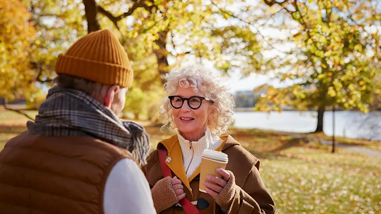 Två personer står i höstskog och dricker kaffe och samtalar.