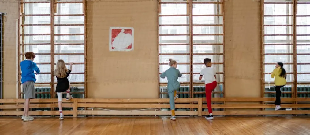 Tre barn stretchar vid ribbstolarna i en idrottssal