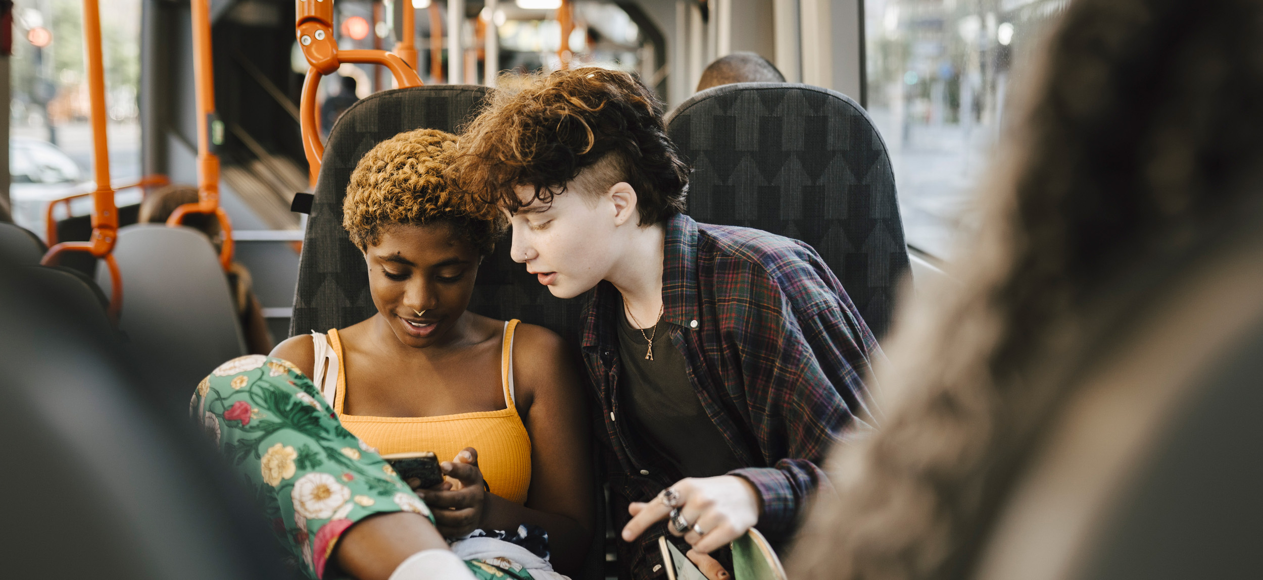 Två ungdomar tittar i samma mobiltelefon på bussen.