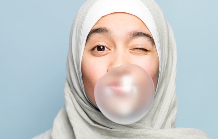 En flicka med slöja blåser en bubbla av rosa tuggummi och blinkar mot kameran.