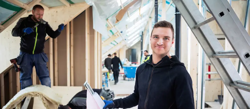 Elektriker på arbetsplats som ler in i kameran.