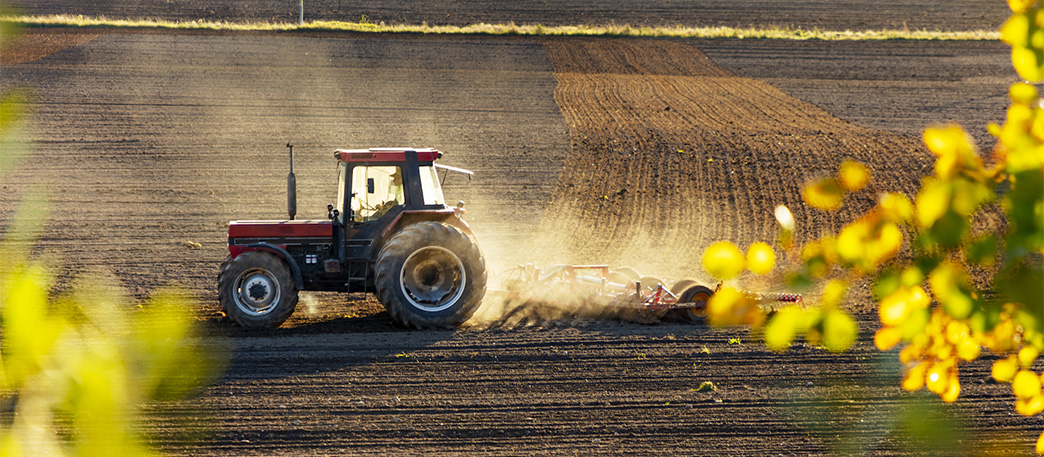 Traktor kör på upplöjd åker. 