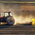 Traktor kör på upplöjd åker. 