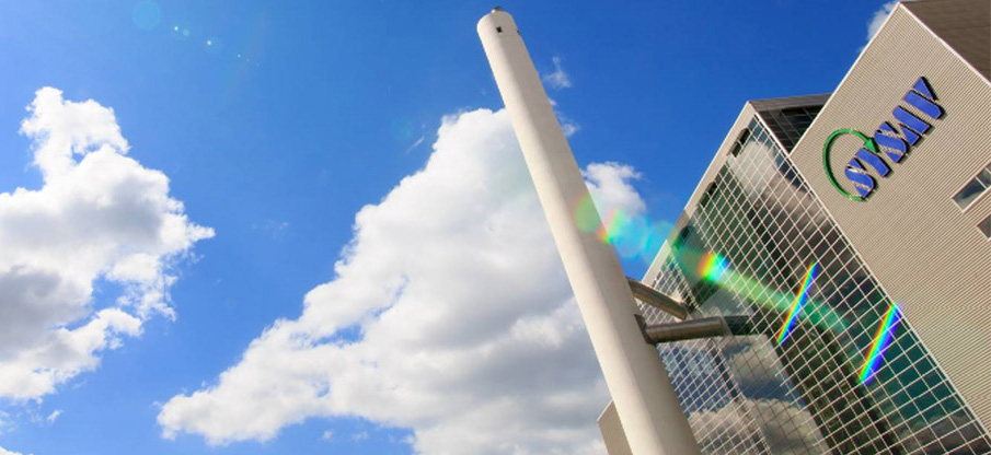Sysavs logga på en byggnad i framgrunden, blå himmel i bakgrunden