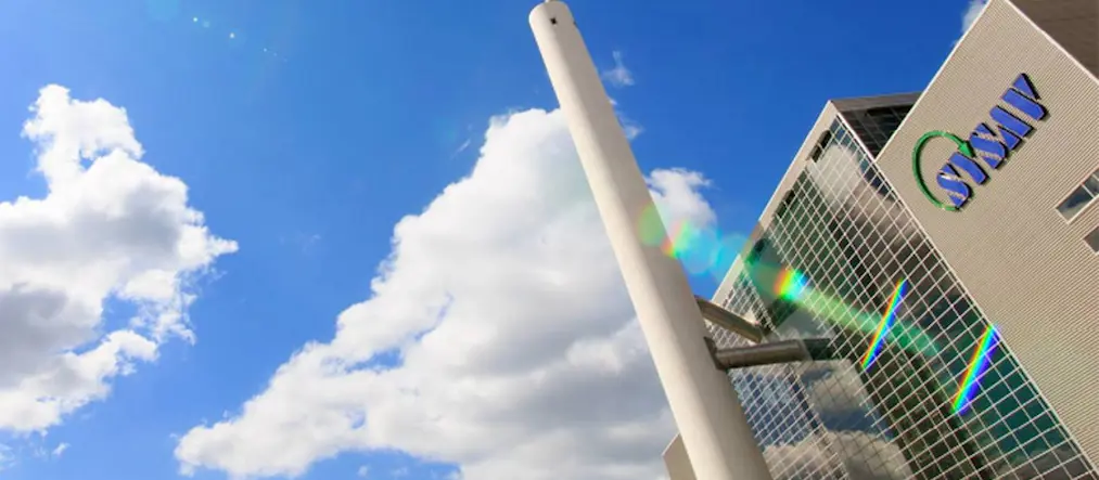 Sysavs logga på en byggnad i framgrunden, blå himmel i bakgrunden