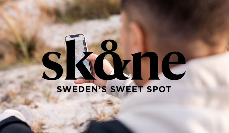 En man håller i en mobiltelefon. På skärmen syns en karta över Skåne. Text i bild: Skåne, Sweden's sweet spot. 