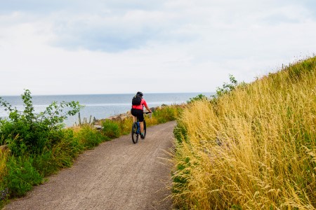 Kvinna cyklar på cykelled längs kusten.