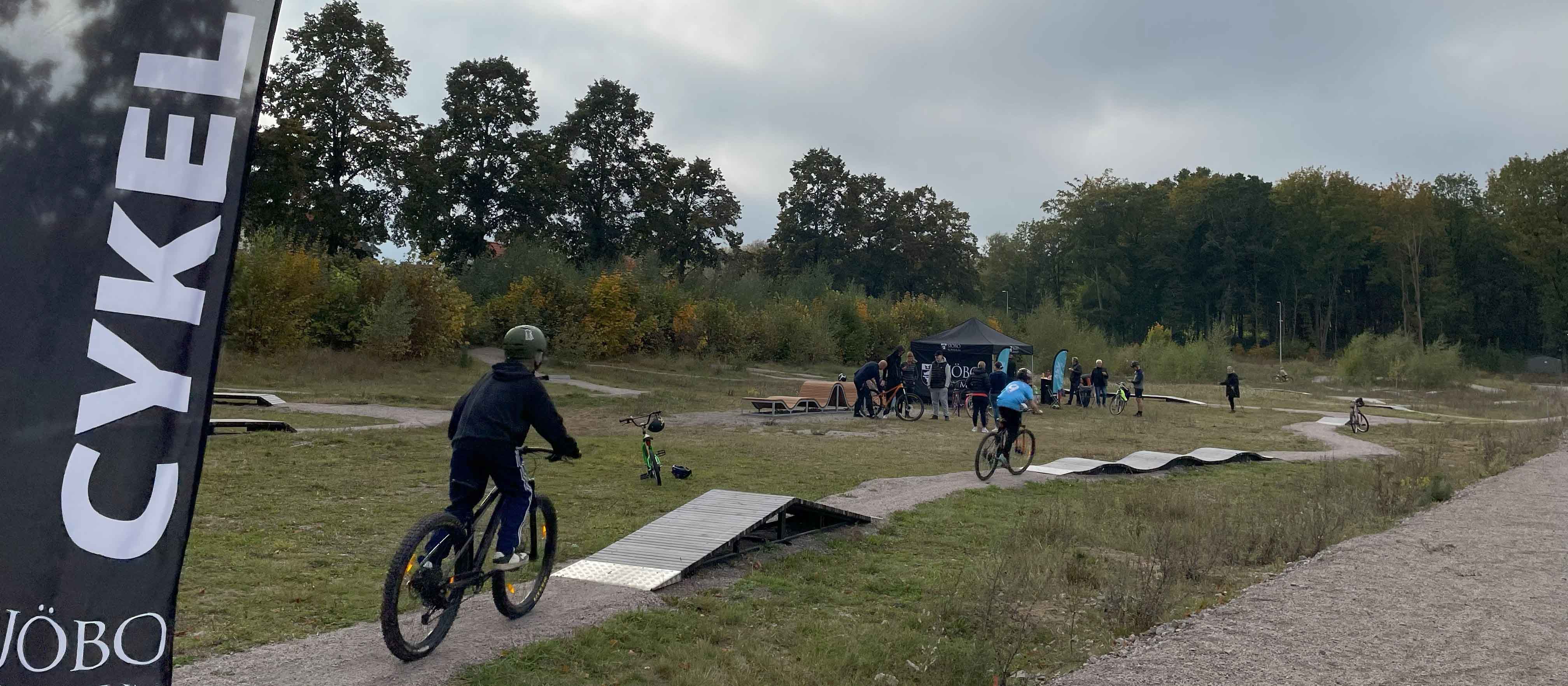 Två barn cyklar på träbana som slingrar sig fram i naturen.