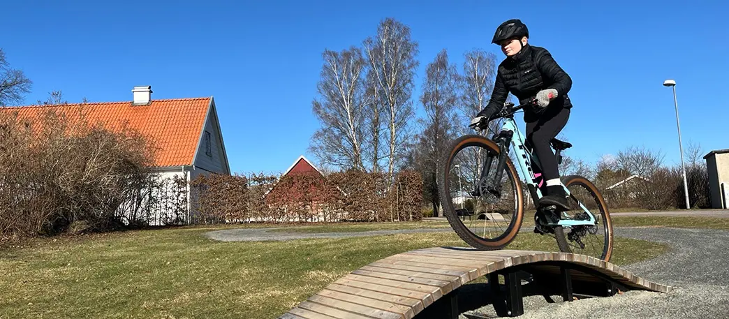 Flicka cyklar över hinder byggt i trä. 