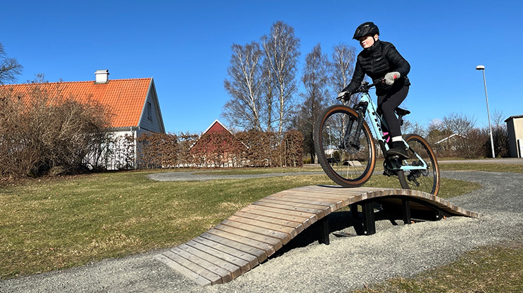 Flicka cyklar över hinder byggt i trä.
