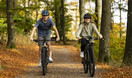 Pojke och flicka cyklar på skogsstig.
