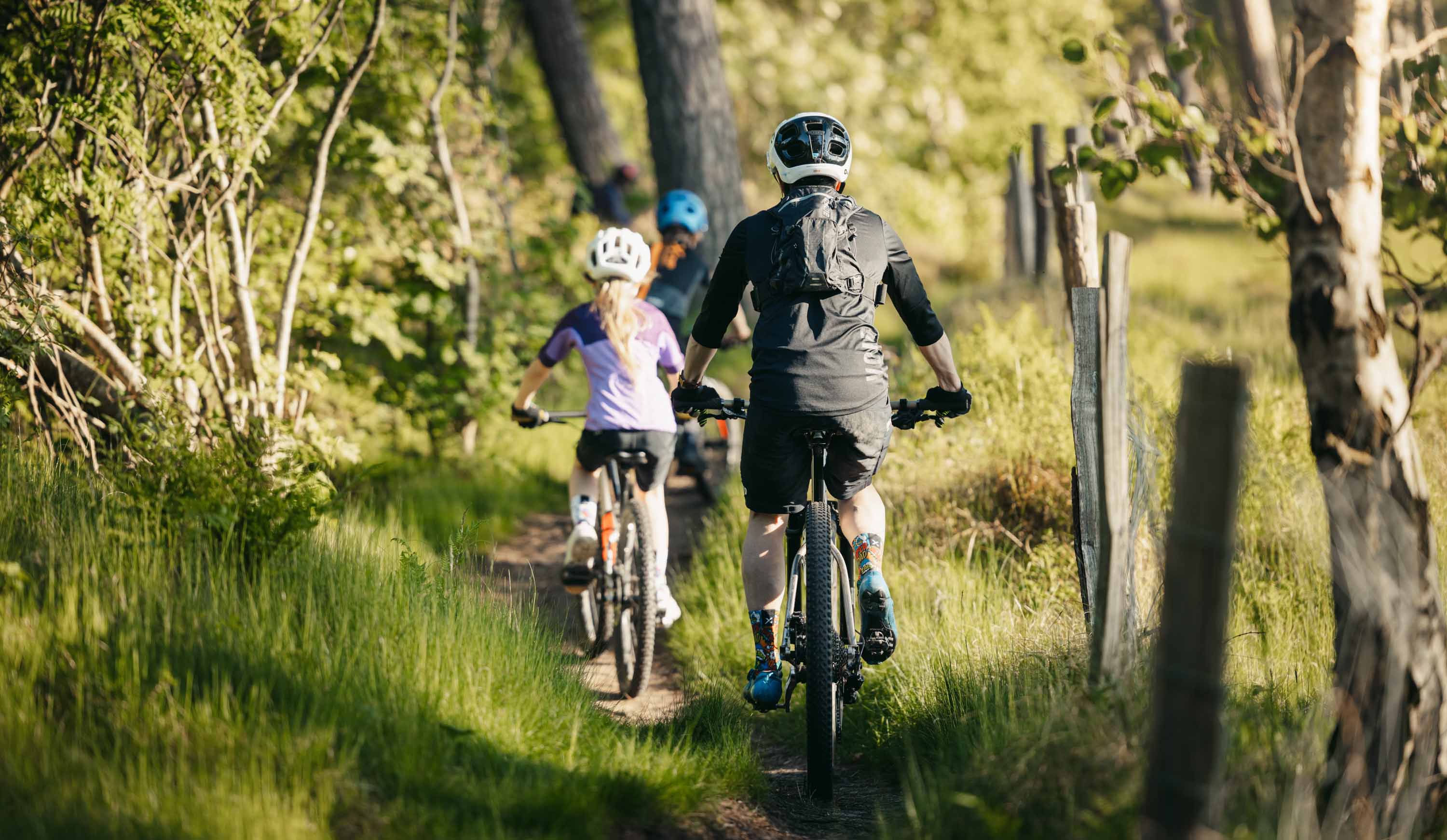 Två barn och en vuxen cyklar på skogsstig.