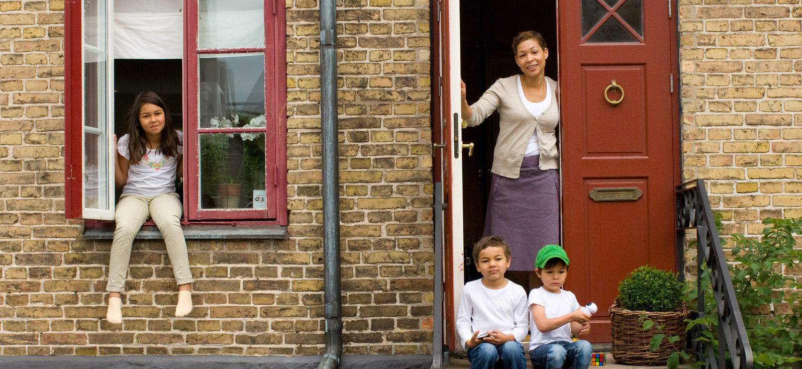 En kvinna och tre barn utanför ytterdörren på sitt gula tegelhus.